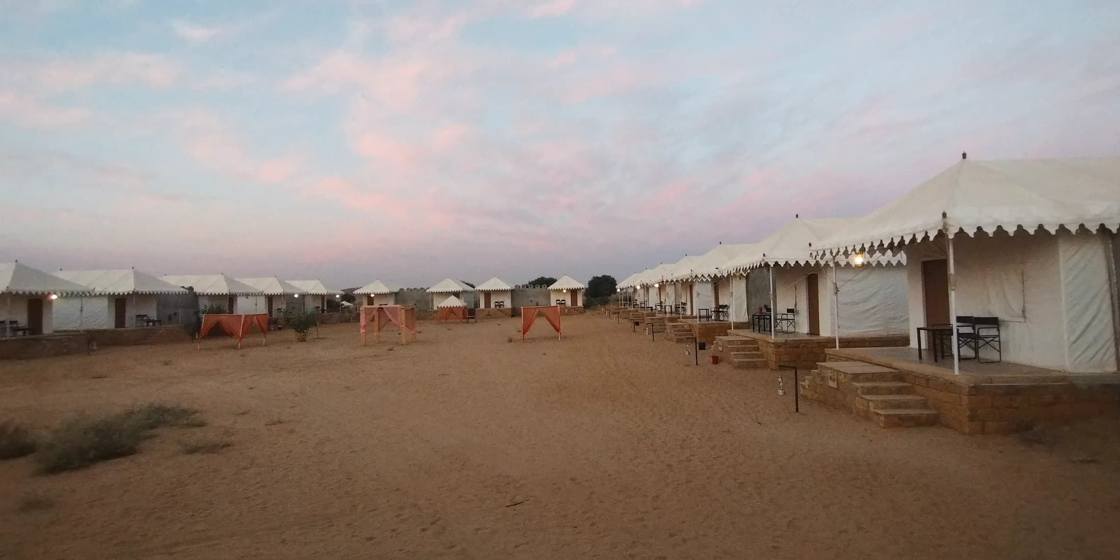 Rows of white Swiss tents at a desert camp near Jaisalmer under an evening sky